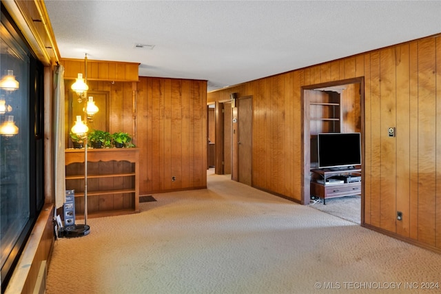 unfurnished living room featuring light carpet, a textured ceiling, and wooden walls