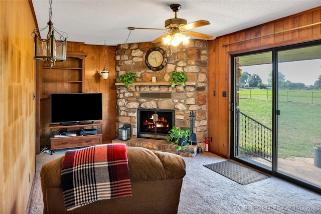 carpeted living room with a textured ceiling, a stone fireplace, wooden walls, and ceiling fan with notable chandelier