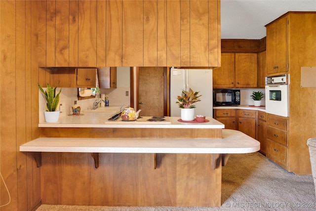 kitchen with kitchen peninsula, a kitchen breakfast bar, white appliances, light colored carpet, and sink