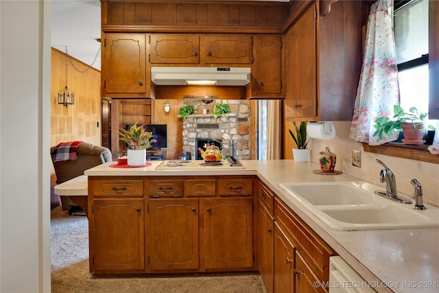 kitchen with light carpet, kitchen peninsula, white appliances, sink, and a stone fireplace