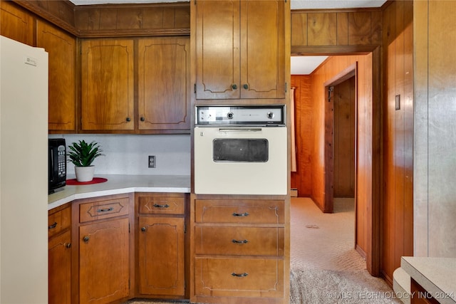 kitchen featuring wood walls, light colored carpet, and white appliances