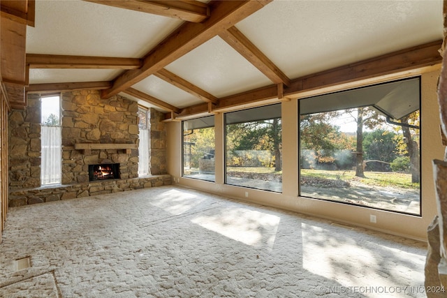 unfurnished living room featuring a stone fireplace, carpet floors, a textured ceiling, and vaulted ceiling with beams