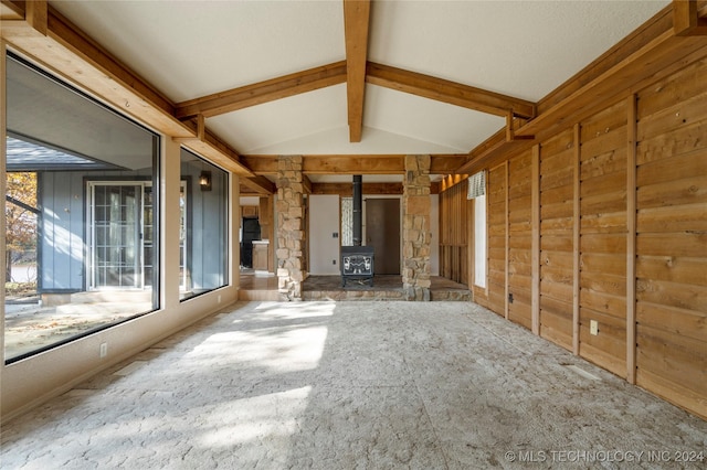 unfurnished living room featuring a wood stove, carpet, a healthy amount of sunlight, and vaulted ceiling with beams