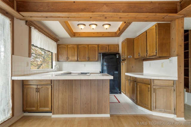 kitchen featuring black refrigerator, light wood-type flooring, tile countertops, and tasteful backsplash