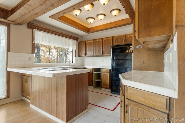 kitchen featuring decorative backsplash, kitchen peninsula, tile countertops, and black fridge