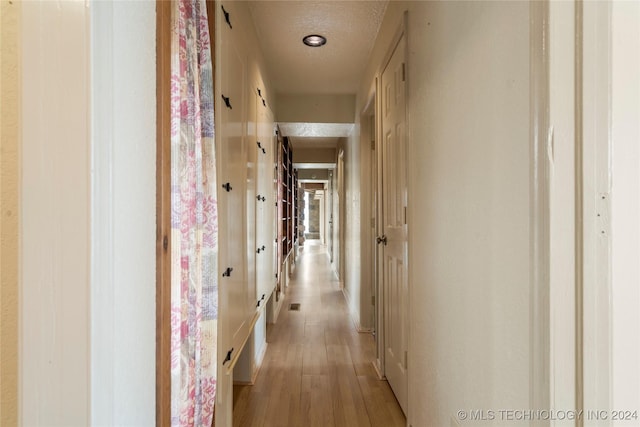 corridor featuring a textured ceiling and light hardwood / wood-style floors