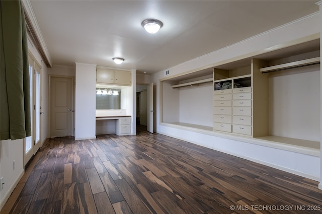 unfurnished living room featuring a healthy amount of sunlight, dark hardwood / wood-style flooring, built in desk, and ornamental molding