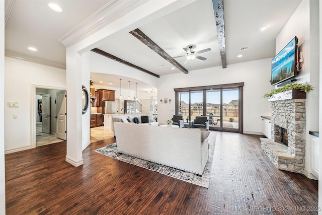 living room featuring dark wood-type flooring, a stone fireplace, ceiling fan, ornamental molding, and beam ceiling