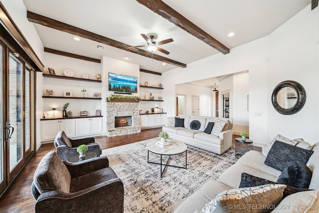 living room with ceiling fan, beam ceiling, built in features, dark hardwood / wood-style floors, and a stone fireplace