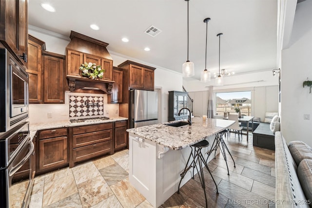 kitchen with sink, stainless steel appliances, decorative light fixtures, a kitchen bar, and a kitchen island with sink