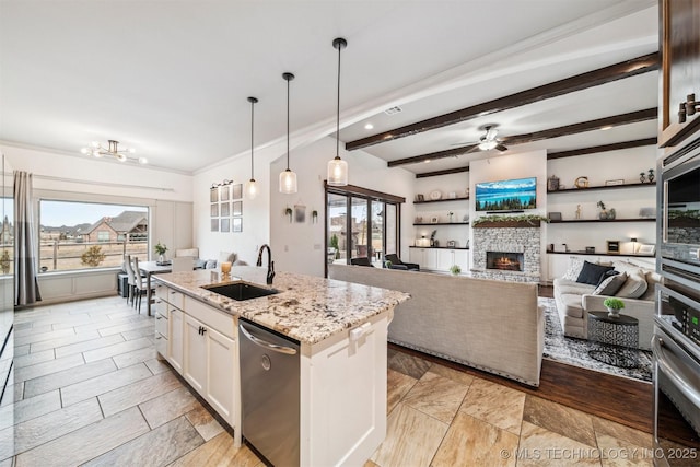 kitchen with light stone countertops, stainless steel appliances, sink, a center island with sink, and white cabinetry