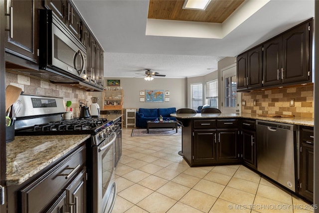 kitchen with a raised ceiling, ceiling fan, decorative backsplash, appliances with stainless steel finishes, and kitchen peninsula