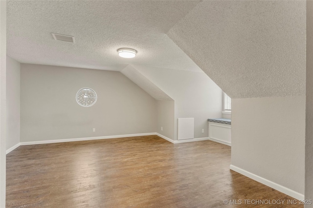 bonus room with wood-type flooring, lofted ceiling, and a textured ceiling