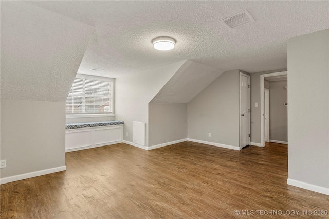 bonus room with wood-type flooring, vaulted ceiling, and a textured ceiling