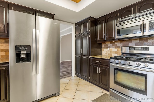 kitchen featuring appliances with stainless steel finishes, backsplash, light tile patterned floors, dark brown cabinetry, and light stone countertops