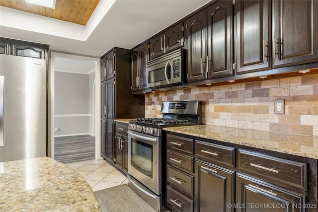 kitchen featuring tasteful backsplash, light tile patterned floors, light stone counters, stainless steel appliances, and dark brown cabinets