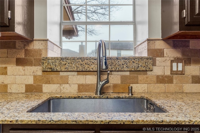 kitchen with dark brown cabinetry, sink, light stone counters, and decorative backsplash