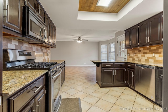 kitchen featuring stainless steel appliances, a raised ceiling, light tile patterned floors, and dark brown cabinetry