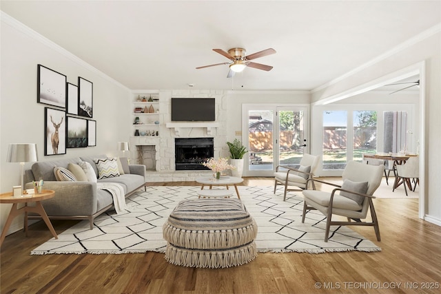 living room with built in shelves, ceiling fan, hardwood / wood-style floors, a fireplace, and ornamental molding