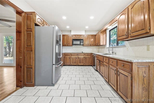 kitchen with sink, decorative backsplash, ceiling fan, appliances with stainless steel finishes, and light stone counters