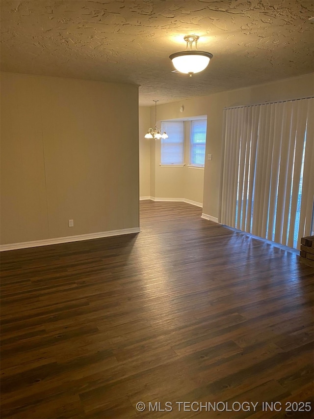 spare room featuring a chandelier, dark wood-type flooring, and a textured ceiling