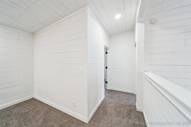 corridor with wooden walls, dark carpet, and vaulted ceiling