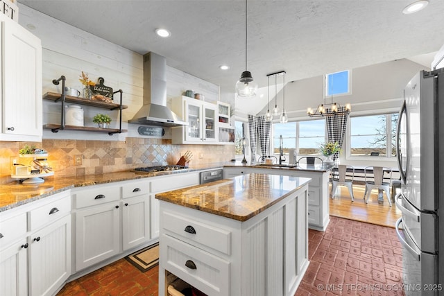 kitchen with light stone countertops, stainless steel appliances, wall chimney range hood, white cabinetry, and a kitchen island