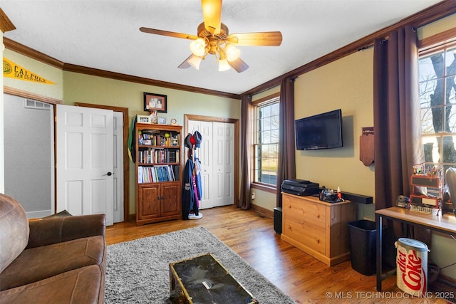 living room with ceiling fan, light hardwood / wood-style floors, ornamental molding, and a textured ceiling