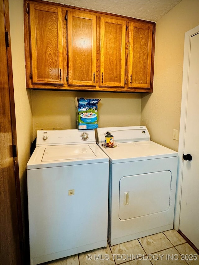 laundry area featuring washing machine and dryer, cabinets, light tile patterned flooring, and a textured ceiling