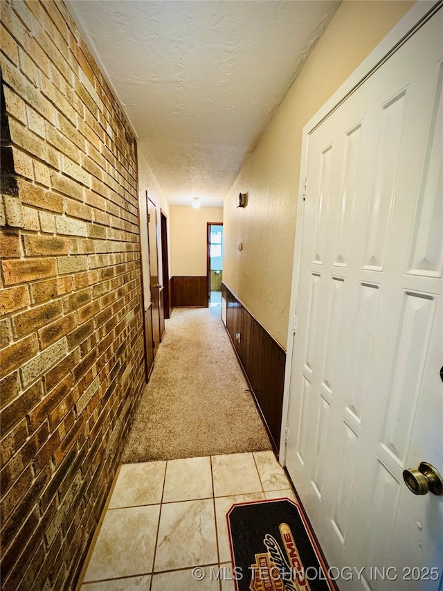 hallway with light colored carpet, brick wall, wood walls, and a textured ceiling