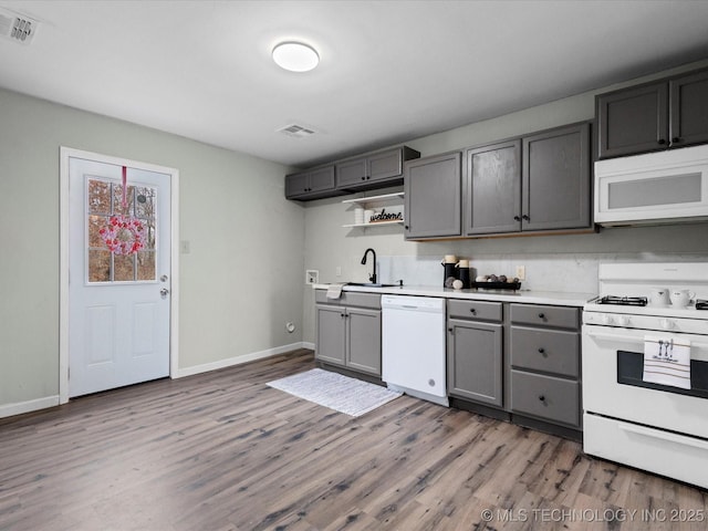 kitchen with backsplash, gray cabinetry, white appliances, sink, and hardwood / wood-style flooring