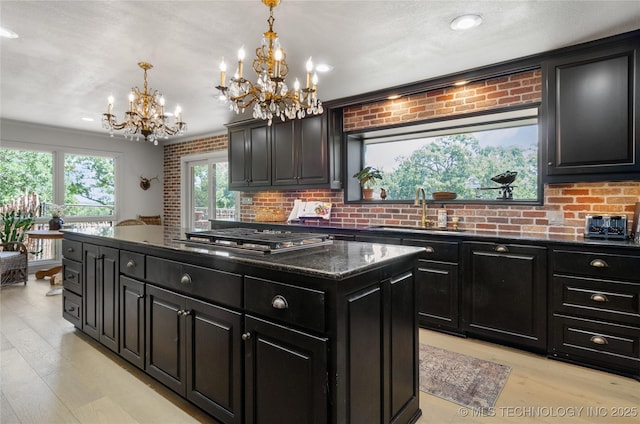 kitchen featuring stainless steel gas stovetop, sink, hanging light fixtures, a notable chandelier, and light hardwood / wood-style floors