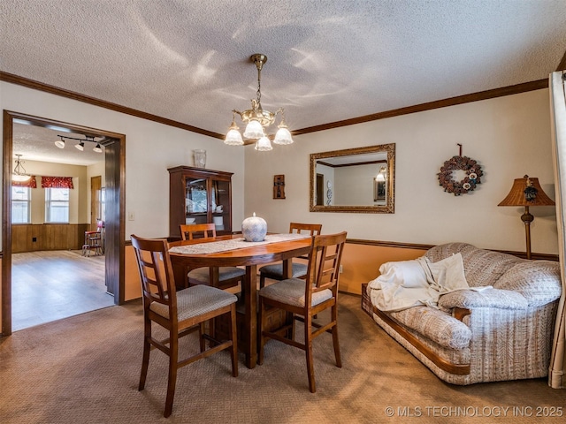 carpeted dining area featuring ornamental molding, a textured ceiling, a notable chandelier, and wood walls