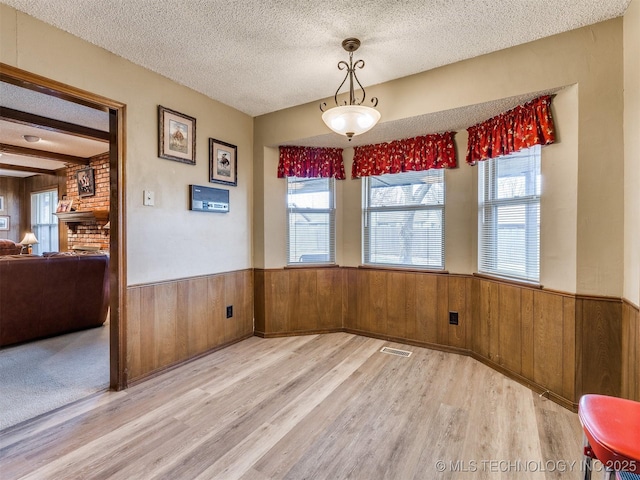 unfurnished dining area with wood walls, light hardwood / wood-style floors, and a textured ceiling