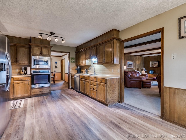 kitchen featuring wood walls, sink, light wood-type flooring, a textured ceiling, and stainless steel appliances