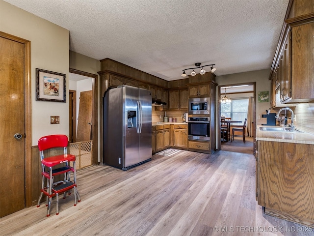 kitchen with a textured ceiling, sink, light wood-type flooring, and stainless steel appliances