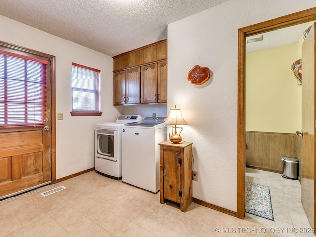 laundry room featuring cabinets, a textured ceiling, wooden walls, and washing machine and clothes dryer