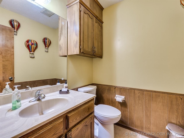 bathroom with wooden walls, vanity, a textured ceiling, and toilet