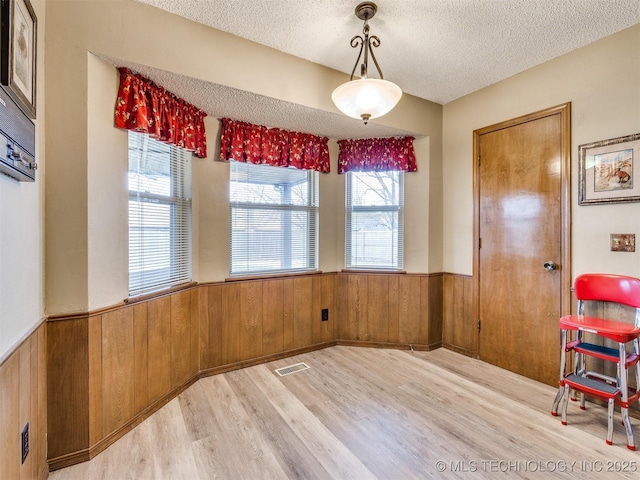 unfurnished dining area featuring wood walls, a textured ceiling, and light wood-type flooring