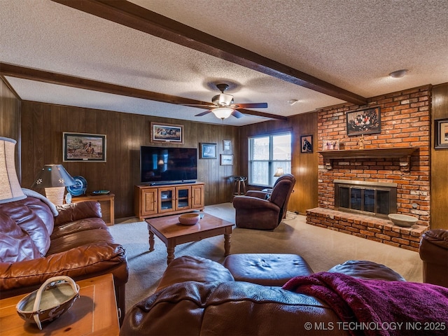 carpeted living room featuring wooden walls, a brick fireplace, ceiling fan, a textured ceiling, and beam ceiling