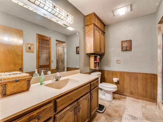 bathroom featuring wood walls, a textured ceiling, toilet, vanity, and a shower with shower door