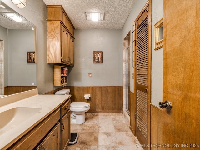 bathroom with vanity, wood walls, toilet, a textured ceiling, and walk in shower