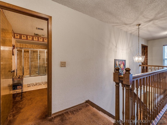 hallway featuring dark carpet, a textured ceiling, and an inviting chandelier