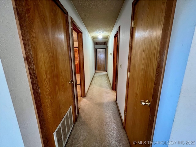 corridor with light colored carpet and a textured ceiling