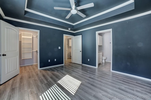 unfurnished bedroom with ceiling fan, ensuite bathroom, a tray ceiling, a walk in closet, and a closet