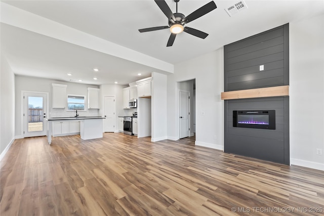 unfurnished living room featuring light wood-type flooring, a large fireplace, and ceiling fan