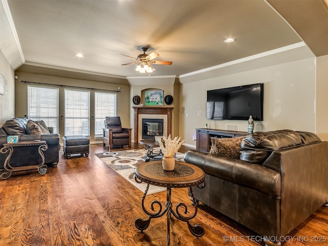 living room with a tile fireplace, ceiling fan, crown molding, and dark hardwood / wood-style floors