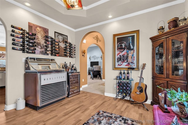 bar with a raised ceiling, wine cooler, light hardwood / wood-style floors, and ornamental molding