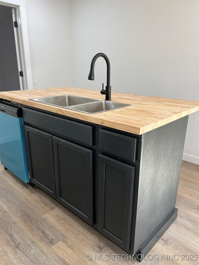 kitchen with stainless steel dishwasher, sink, a center island with sink, light hardwood / wood-style flooring, and butcher block counters