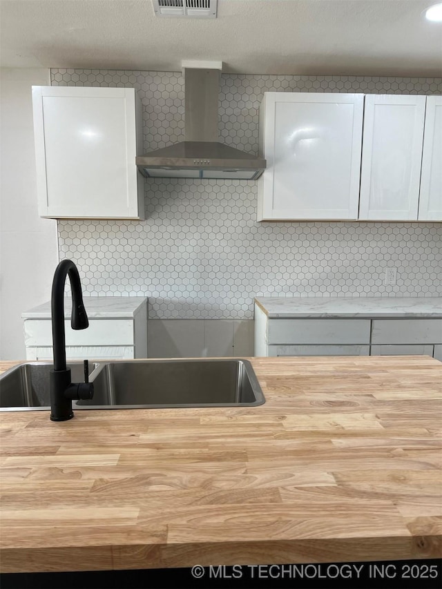 kitchen with decorative backsplash, white cabinetry, sink, and wall chimney exhaust hood